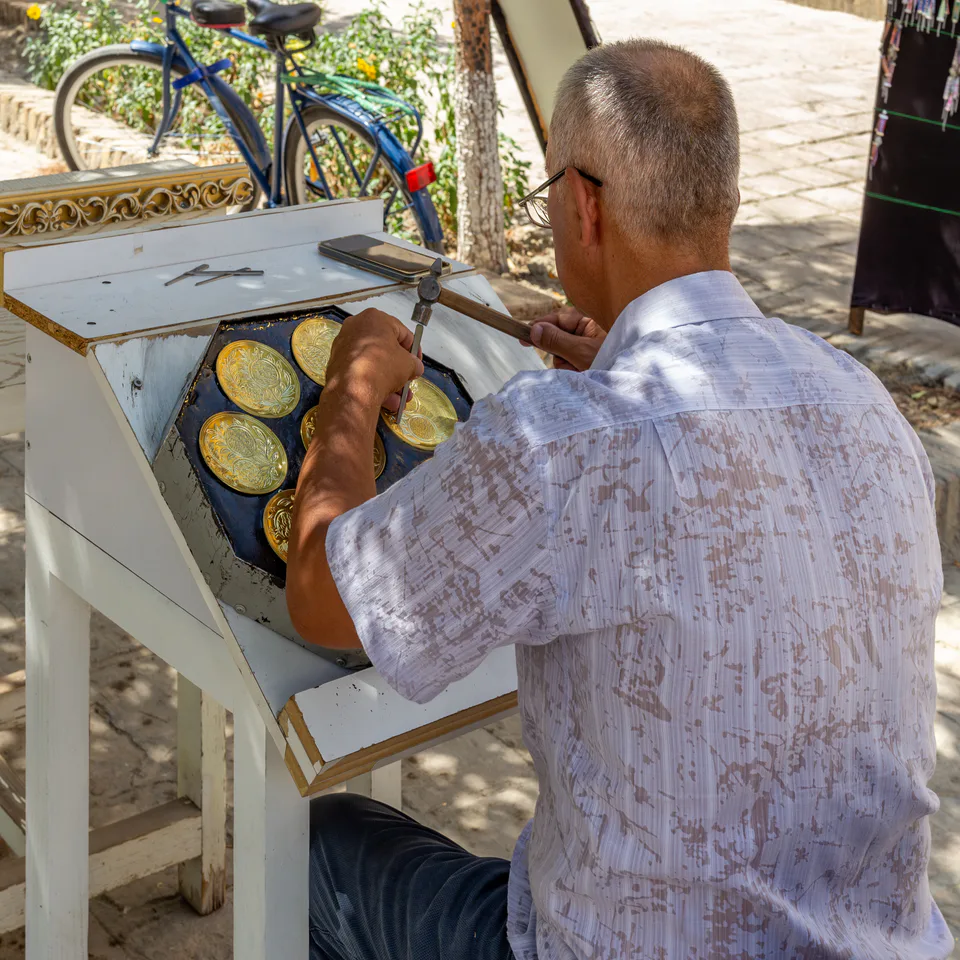 Coppersmith is engraving on plates in Kukeldash medrese yard. Bukhara, Uzbekistan.
