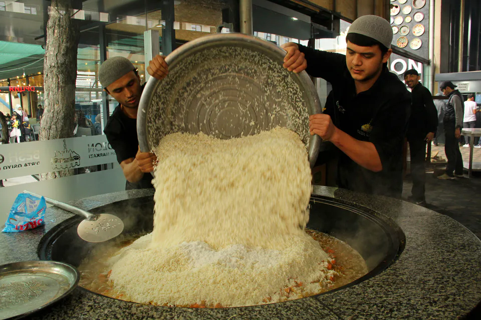 Men pour rice into a cauldron while cooking pilaf at the Tashkent restaurant Besh Qozon
