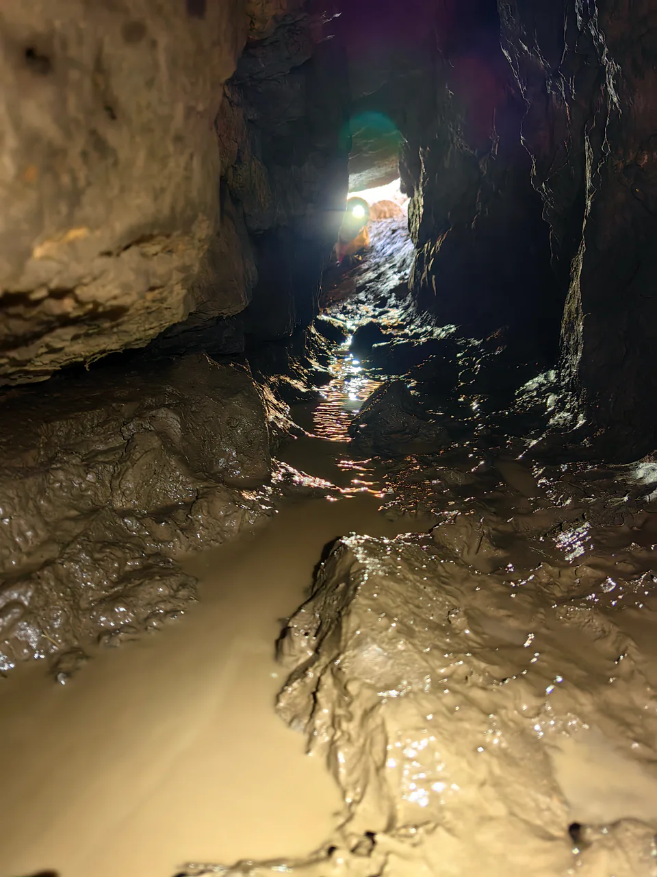 View out, to the entrance, across the first passage of the cave Boybuloq in Uzbekistan, with Marija Studenikina - Maša. It is 7 meters of a low horizontal passage, with mud, water and solid rock here 